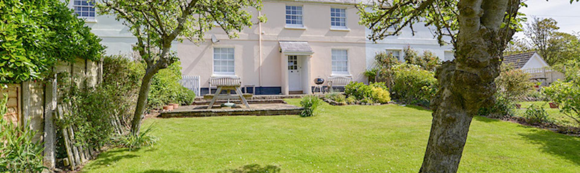 A double-fronted Hope Cove holiday cottage overlooks a large lawn.