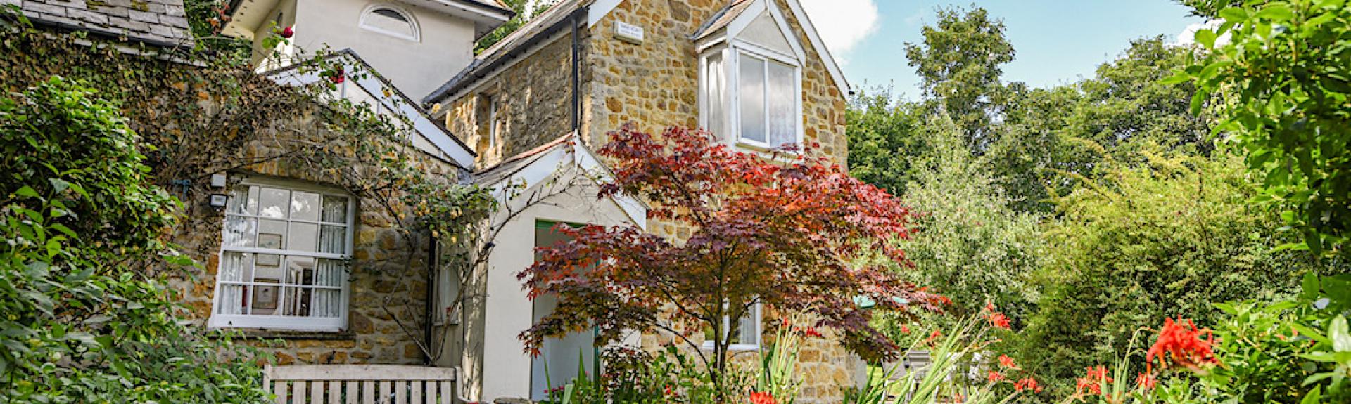 A 2-storey Chideock holiday cottage with a tower surrounded by a flower-filled garden.