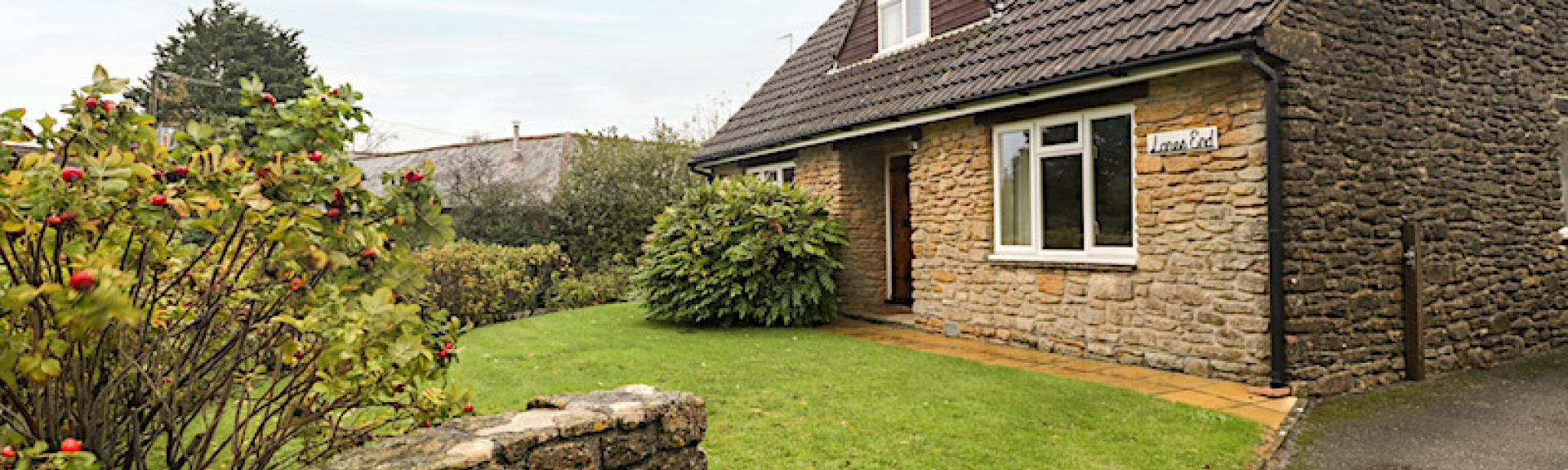 Exterior of a stone-built Dorset chalet bungalow overlooking a front lawn and drive.
