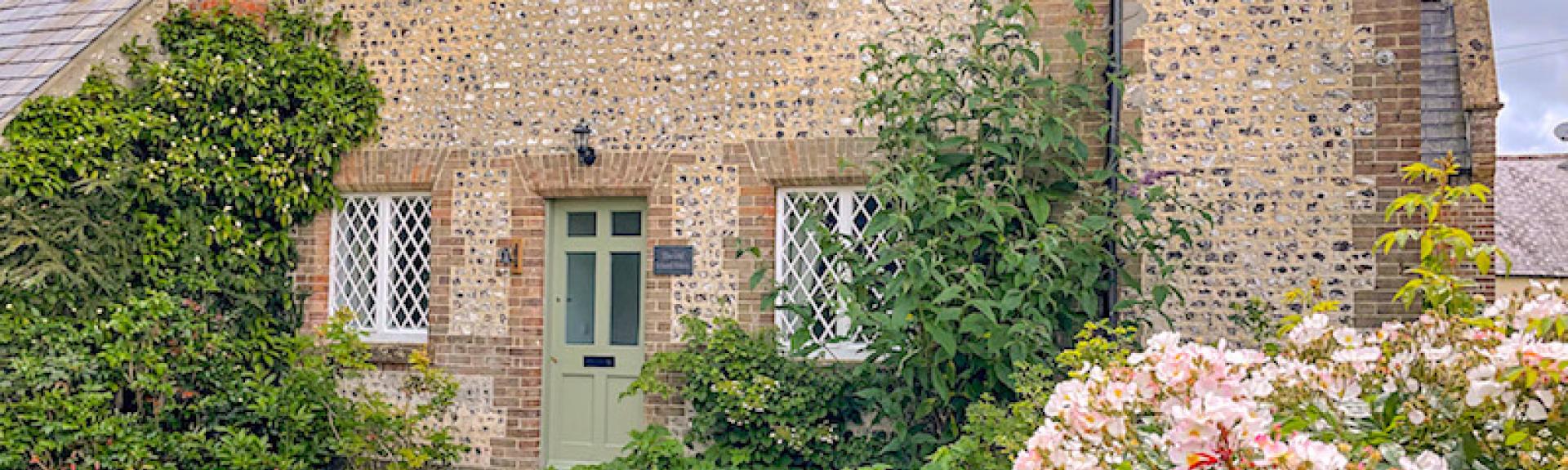 Gable end of a stone-built Dorset holiday cottage overlooking a shrub-filled front garden.
