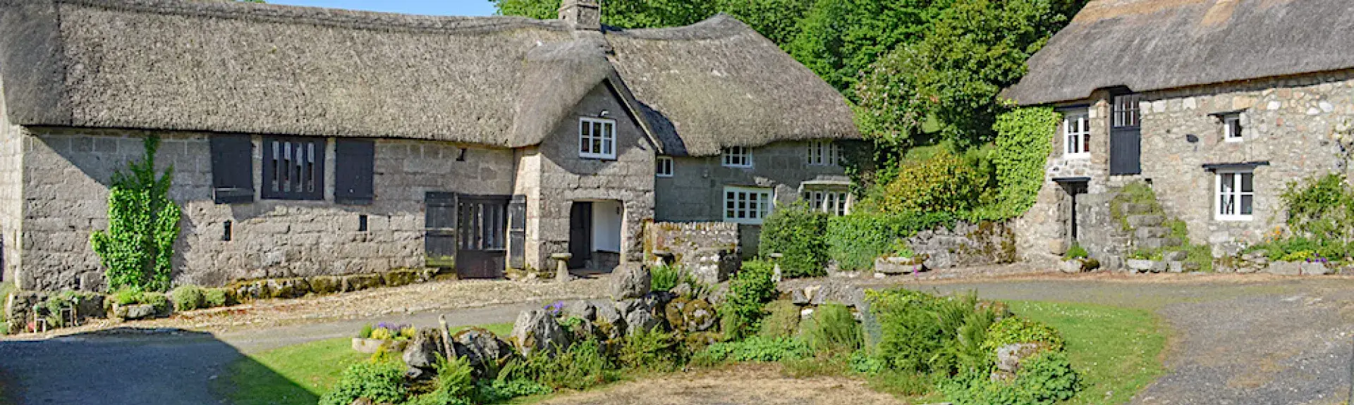 An ancient granite built and thatched Dartmoor longhouse overlooking a lawn.e