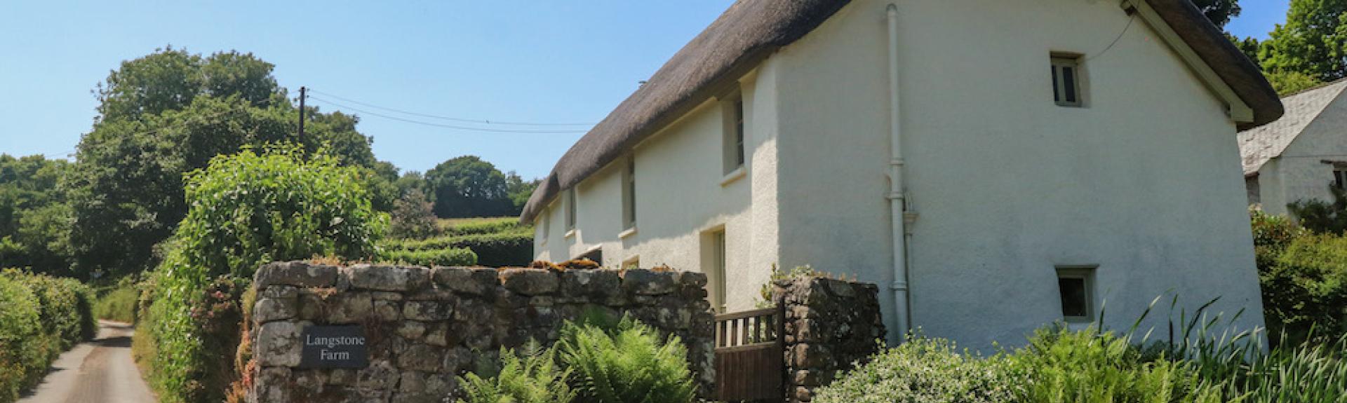 Exterior of a large thatched Dartmoor farmhouse amidst mature gardens