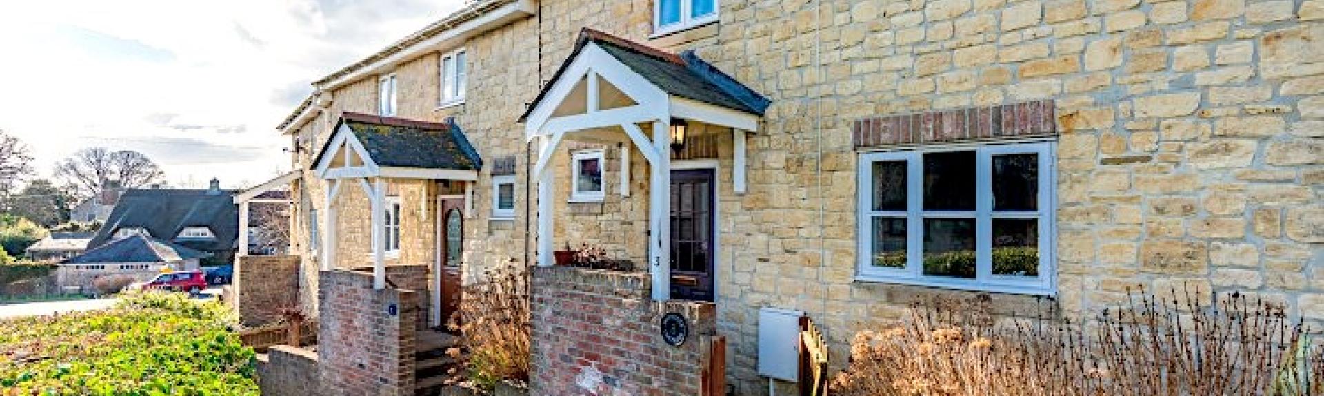 A limestone-built Dorset holiday cottage with a porch and tiny front garden.