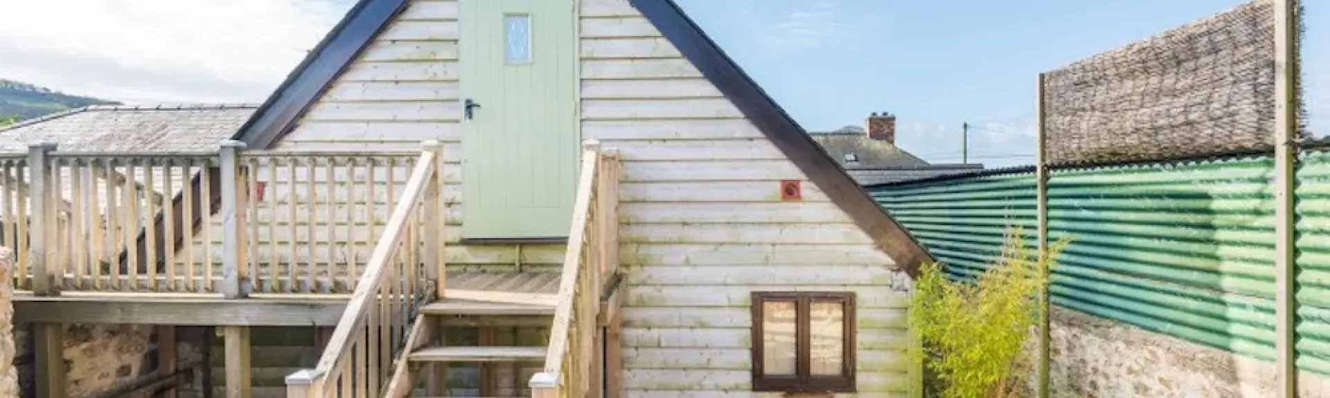 Gable end of a wood panelled Dorset barn conversion with wooden steps to a front door and deck.