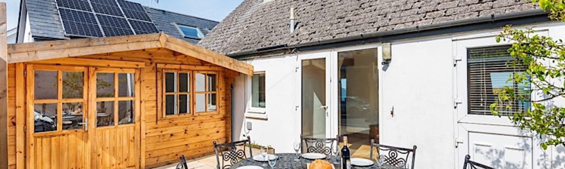 A single-storey holiday cottage overlooks a courtyard with a table laid for a meal