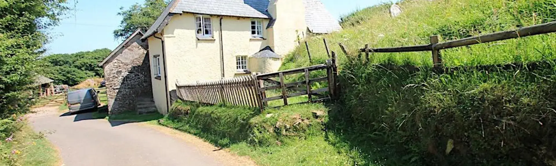 L-shaped exterior of a country cottage with a lawn surrounded by flowering shrubs and bushes.