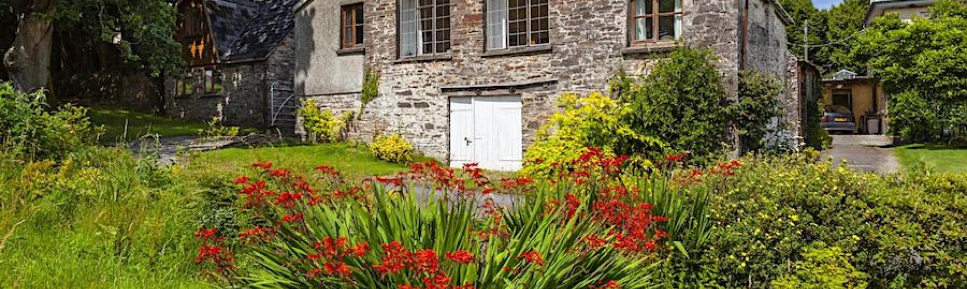 Exterior or a stone-built barn conversion surrounded by a flower-filled garden