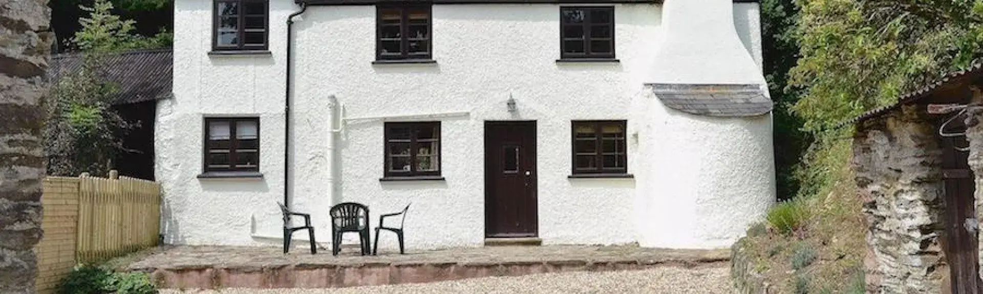 Exterior of an Exmoor country cottage with large chimney in front of tall trees and overlooking a large courtyard.