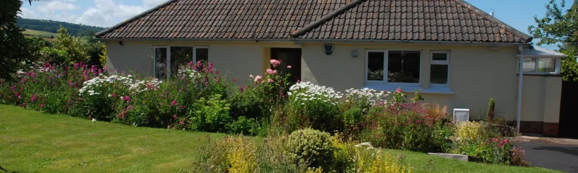 A bungalow sits behind a large lawn with flower-filled borders.
