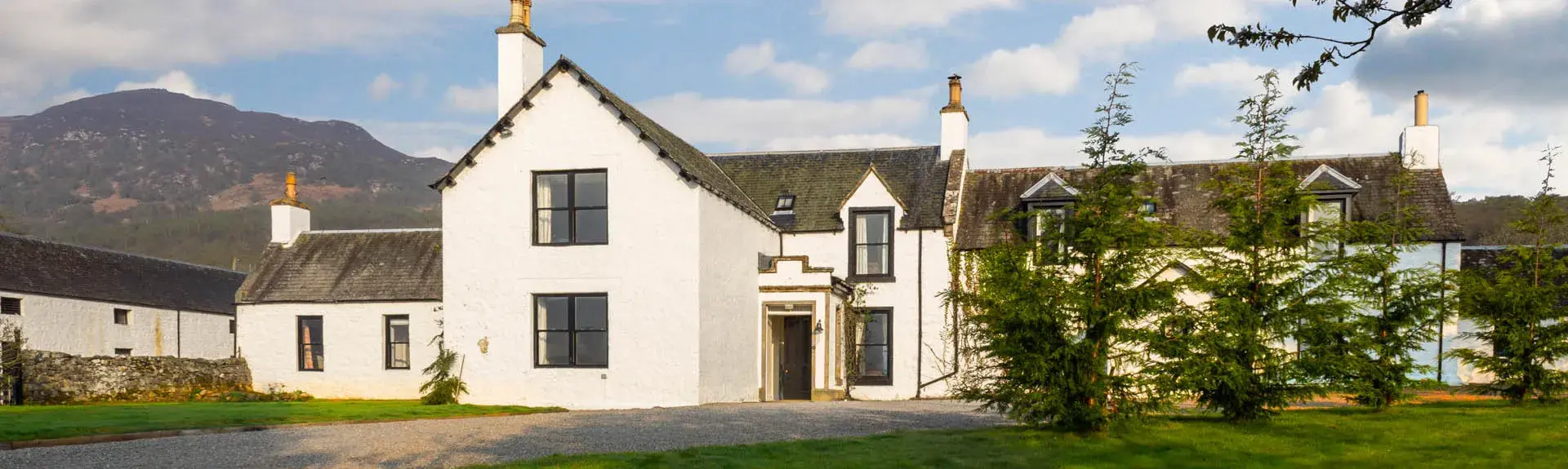 Exterior of a large country house with a Highland mountain in the background. 
