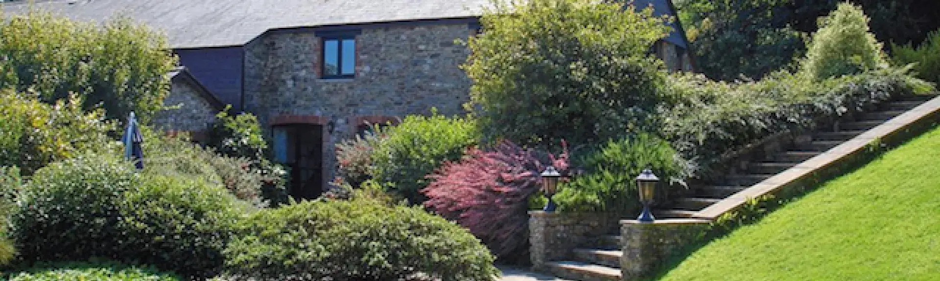 A stone-barn conversion surrounded by mature shrubs and trees.