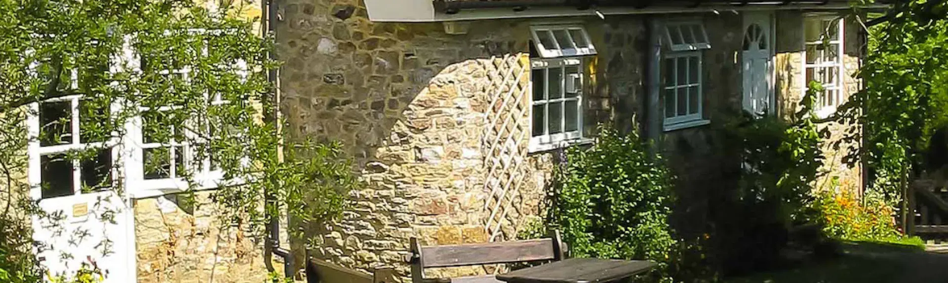 A stone-built holiday cottage with a picnic table patio overlooks a lawn.