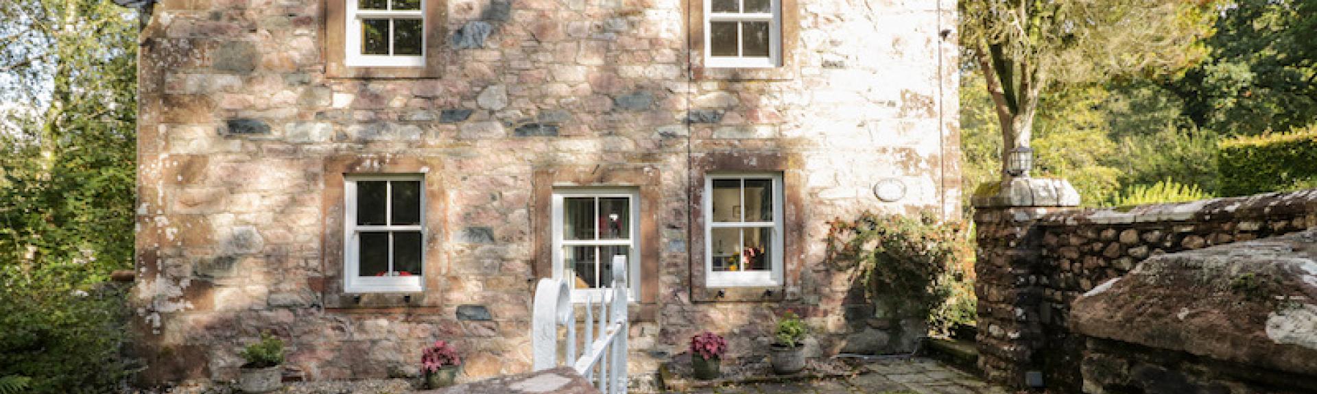 A stone-built, 2-storey cottage in Cumbria overlooks a large lawn.