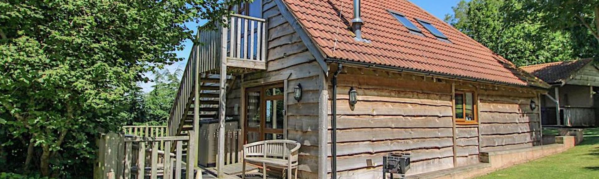 Large timber eco-holiday lodge with a hot tub and tree-lined lawn.