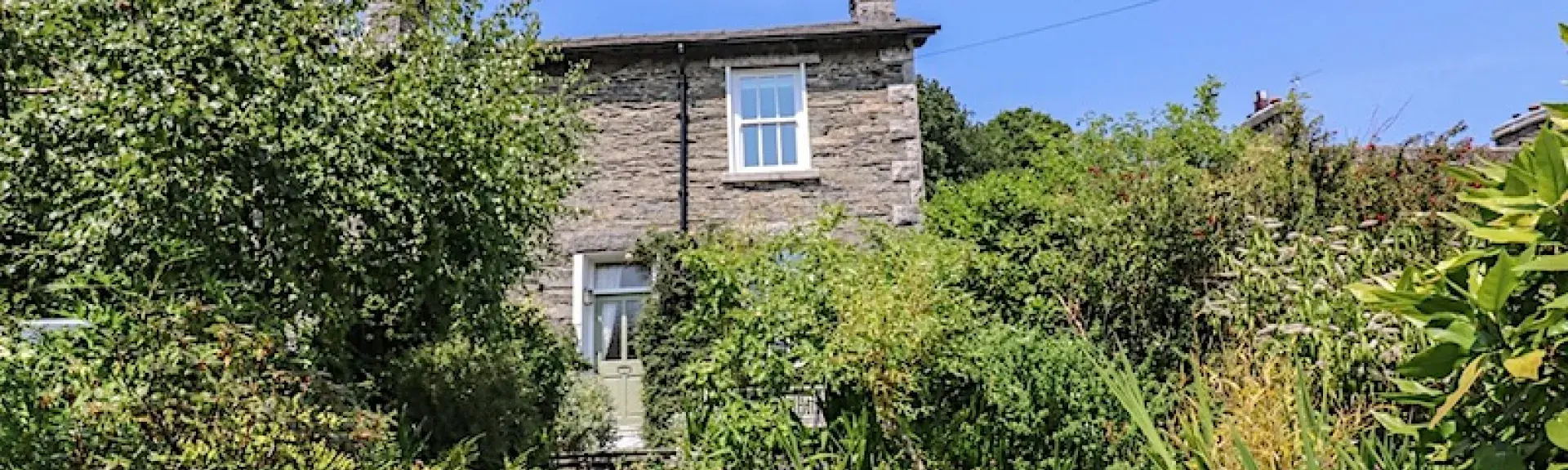A stone-builkt cottage overlooks a garden with mature trees and shrubs.