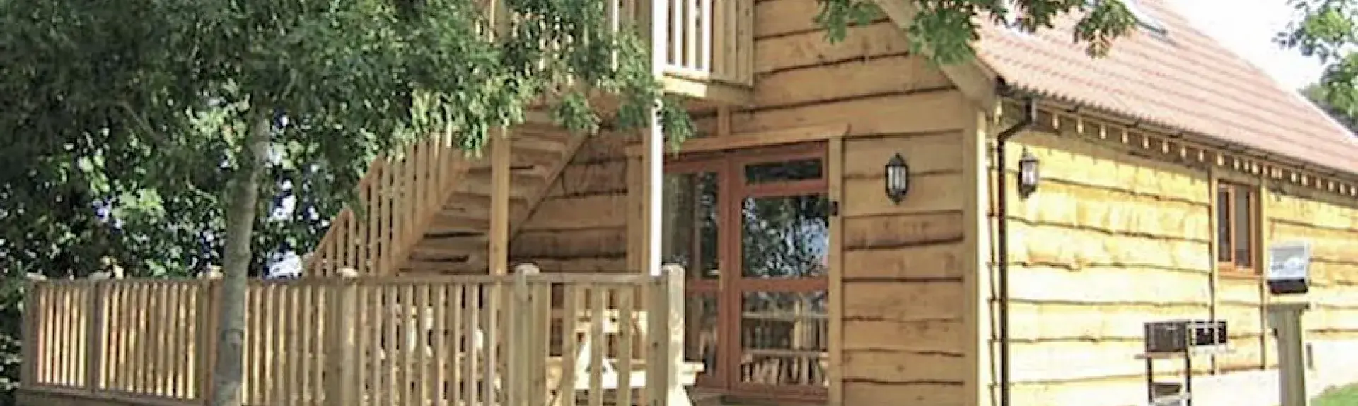 Exterior of a wooden eco-lodge with stairs to the 1st floor and a wide deck.