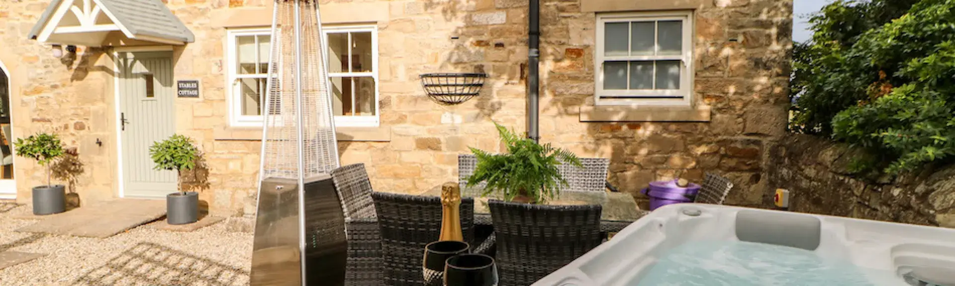 Exterior of a barn conversion overlooking a terrace with a hot tub.