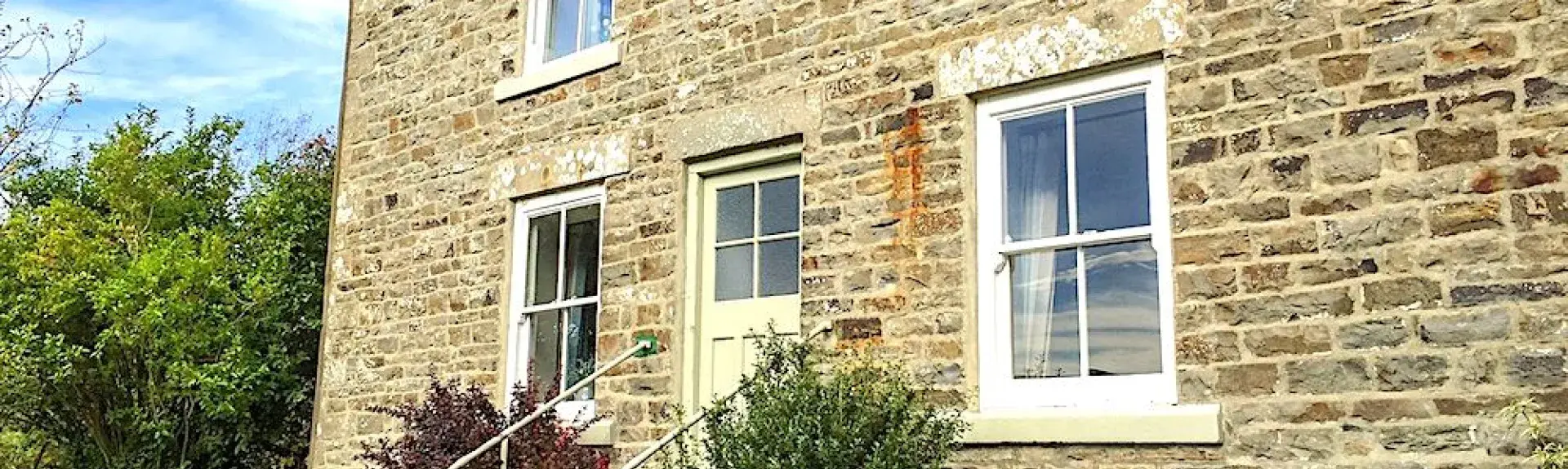2-storey stone-built cottage overlooking a shrub-lined lawn.