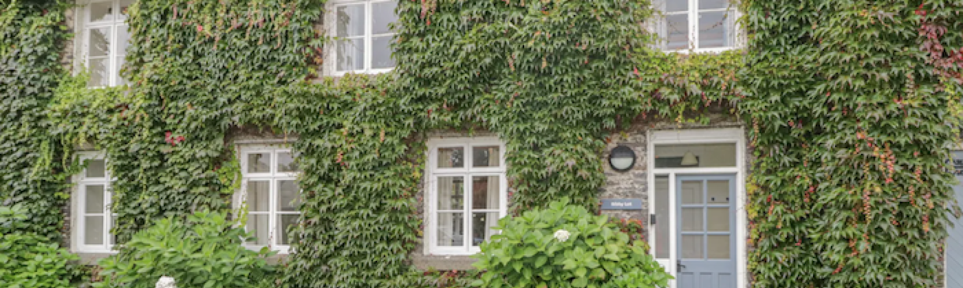 Ivy-clad exterior of a stone holiday cottage in Hawkshead, Cumbria, with a lawn to the front.