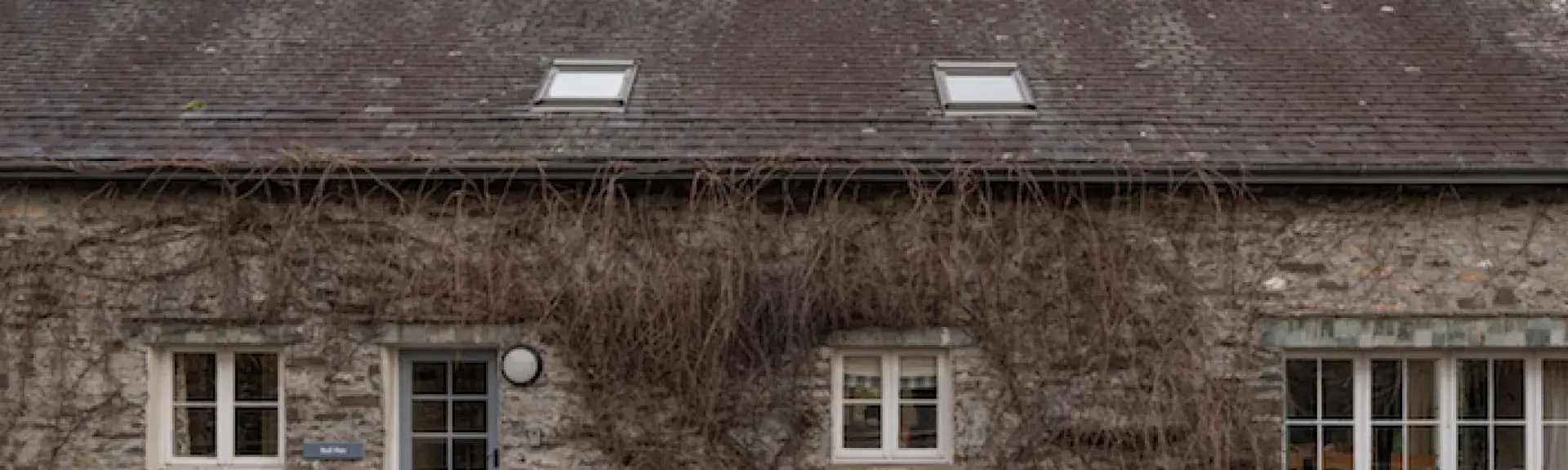 A stone-built, vine-clad barn conversion behind a low stone wall
