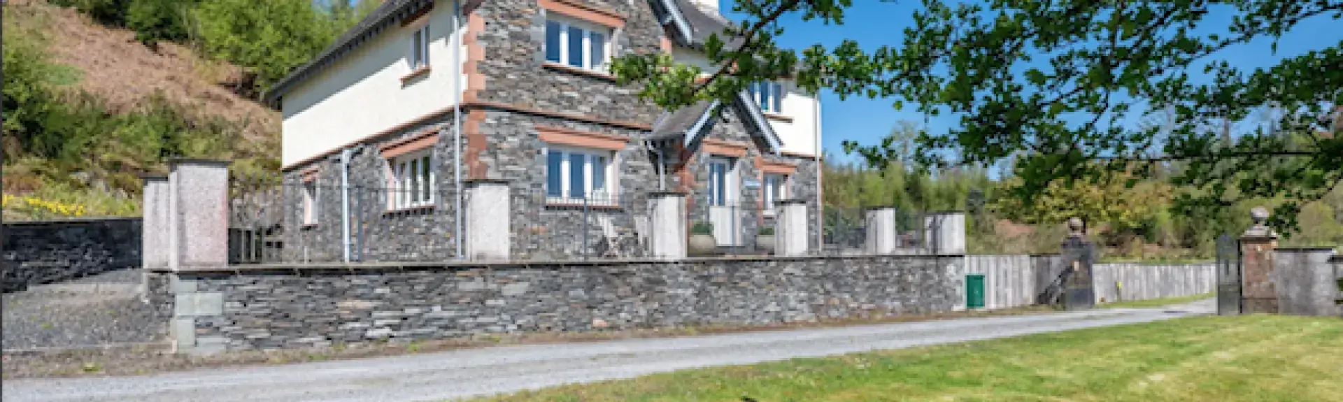 A Large stone-built Lake District lodge overlook a drive and large lawn.