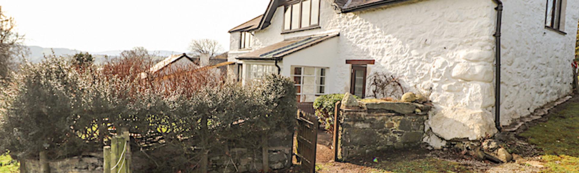 Exterior of a large whitewashed Welsh farmhouse and garden.