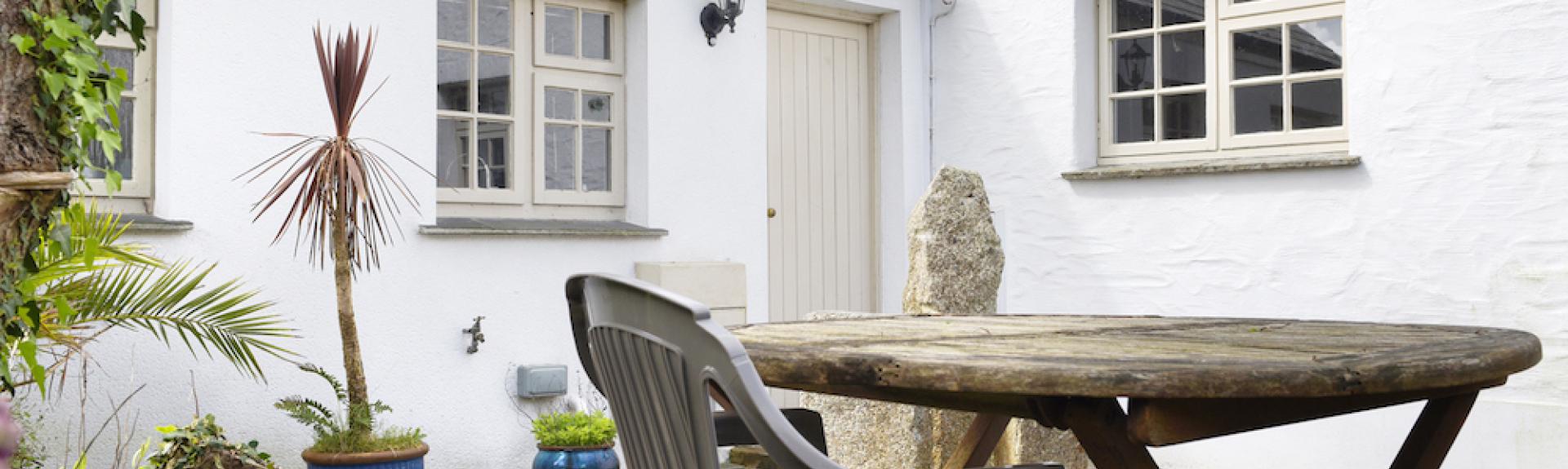 Whitewashed extrior of a Cornish cottage overlooking a courtyard.