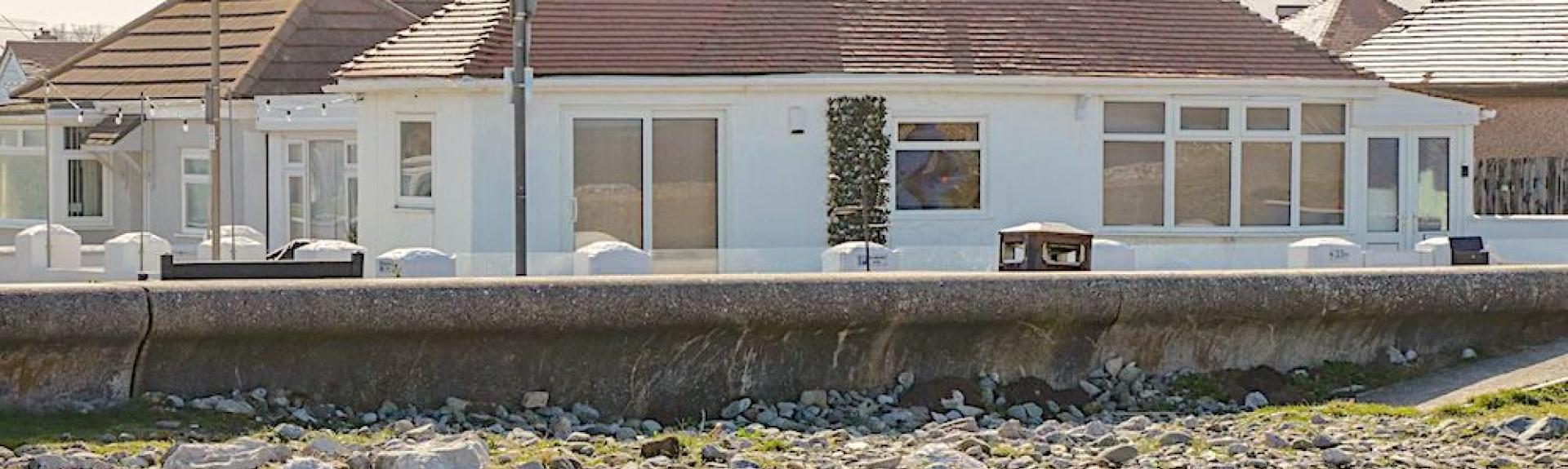 Exteerio of a beachfront chalet bungalow overlooking a sea wall.