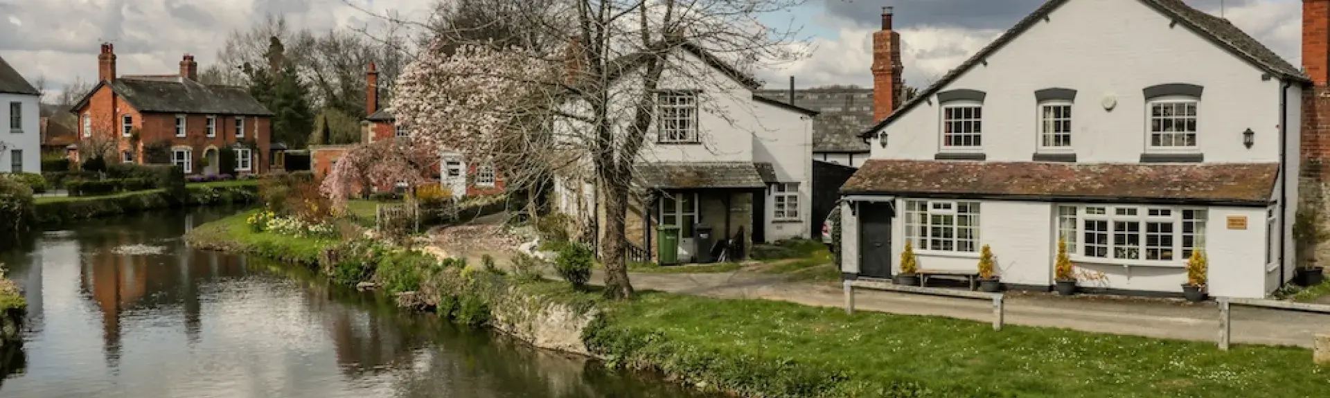 A Herefordshire riverside cottage with bay windows is fronted by a grassy bank down to a wide river.