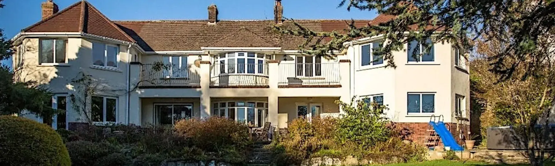 A large house with two bay wings overlooks a shrub-liined lawn.