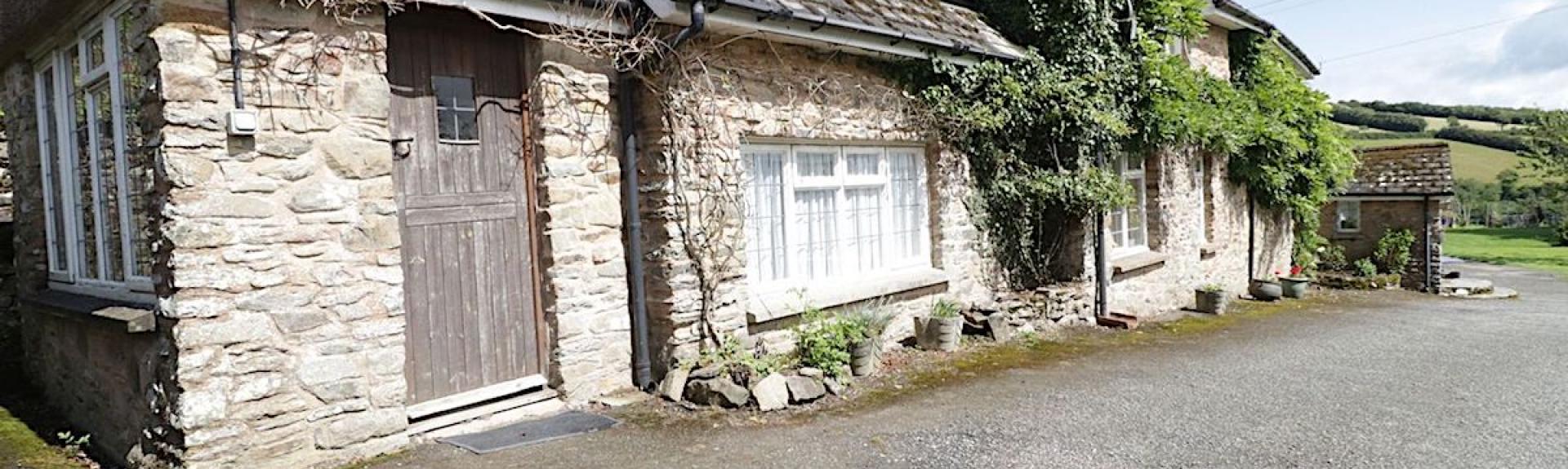 A wisteria-clad, stone-built Exmoor farm cottage surrounded by countryside.