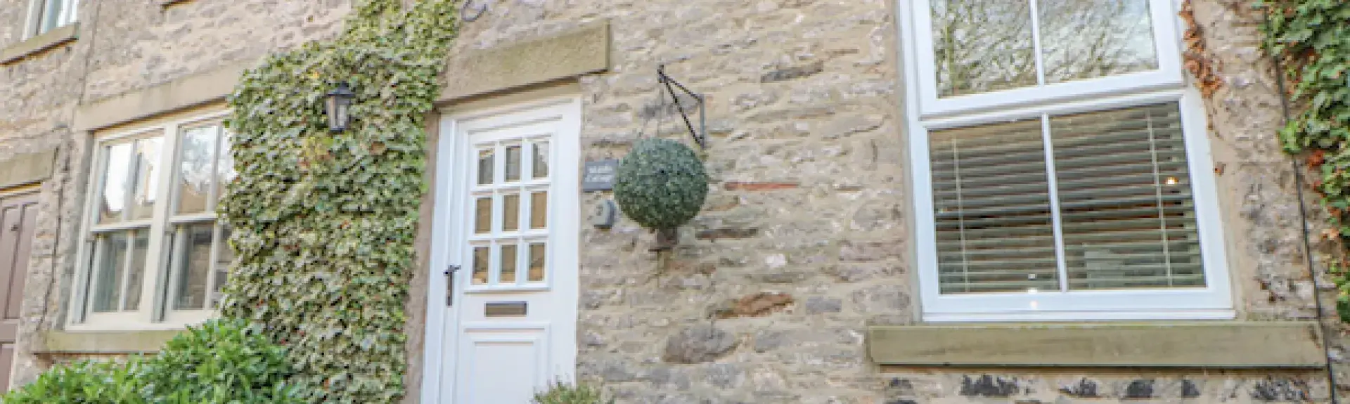 Stone built exterior of a Yorkshire Dales cottage with large zinc plant pots lining the front.