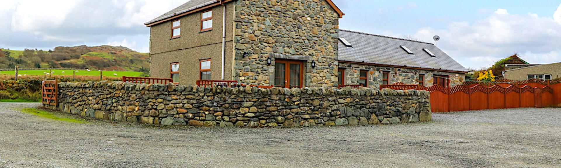 A Welsh stone-built barn conversion surrounded by a low stone wall in a large courtyard.