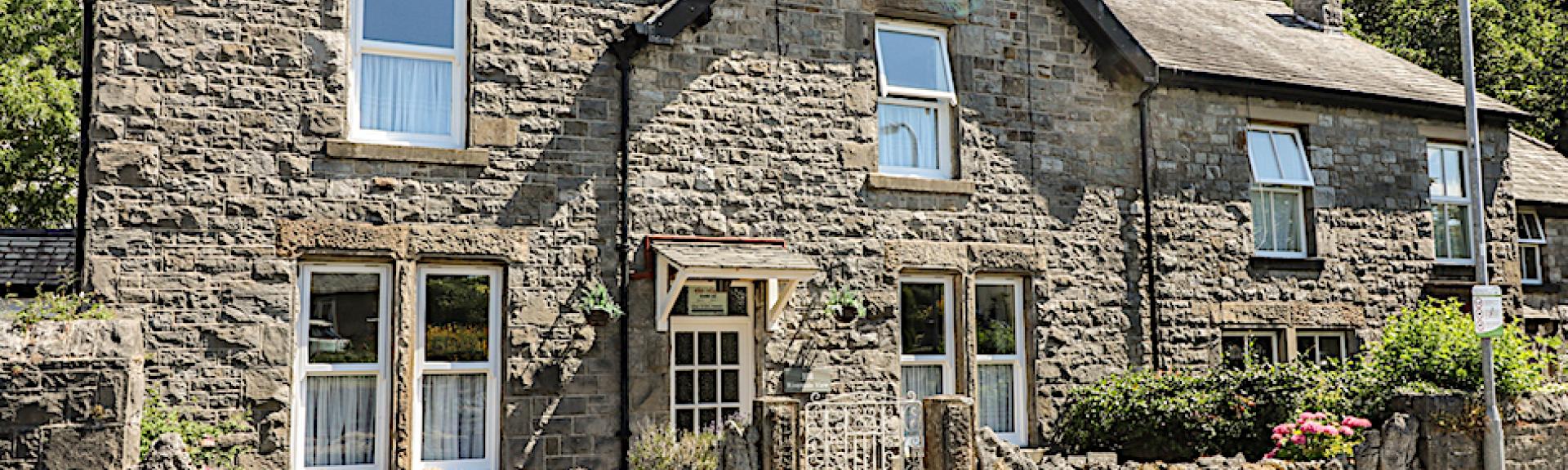 Stone built Cumbrian holiday cottage with a front garden behind a low stone wall.