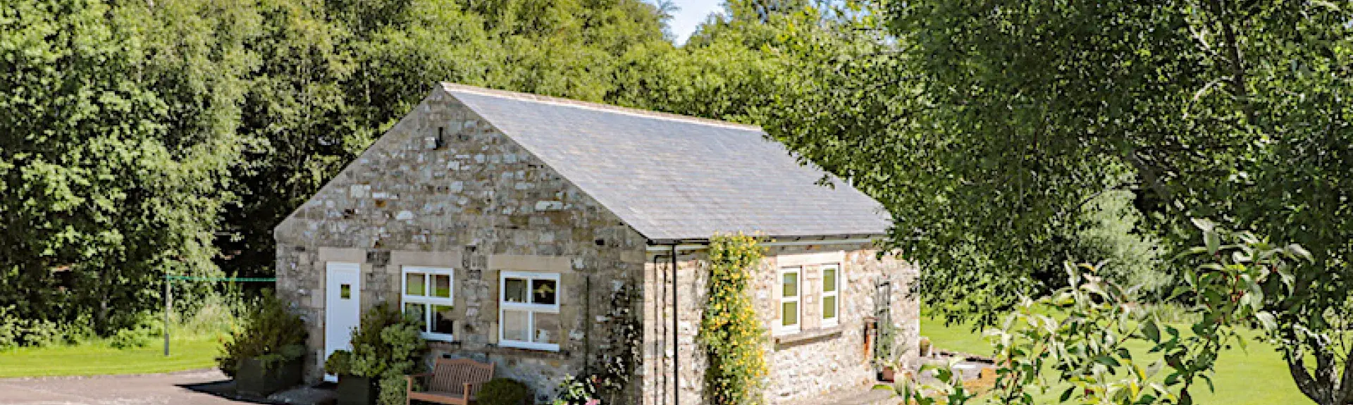 A single storey Northumberland barn conversion surrounded by a large, tree-fringed lawn