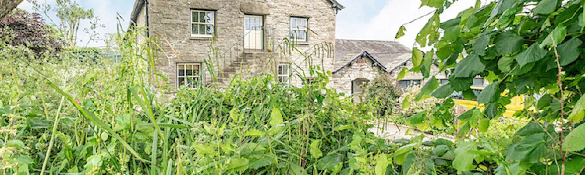 The 3-storey gable end seen through trees of a Cumbrian stone-barn conversion.