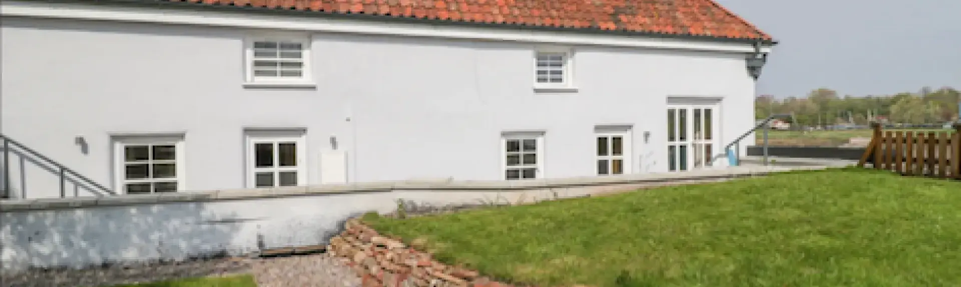 A rural holiday cottage with a terracotta roof sits behind a lawn with a shingled footpath.