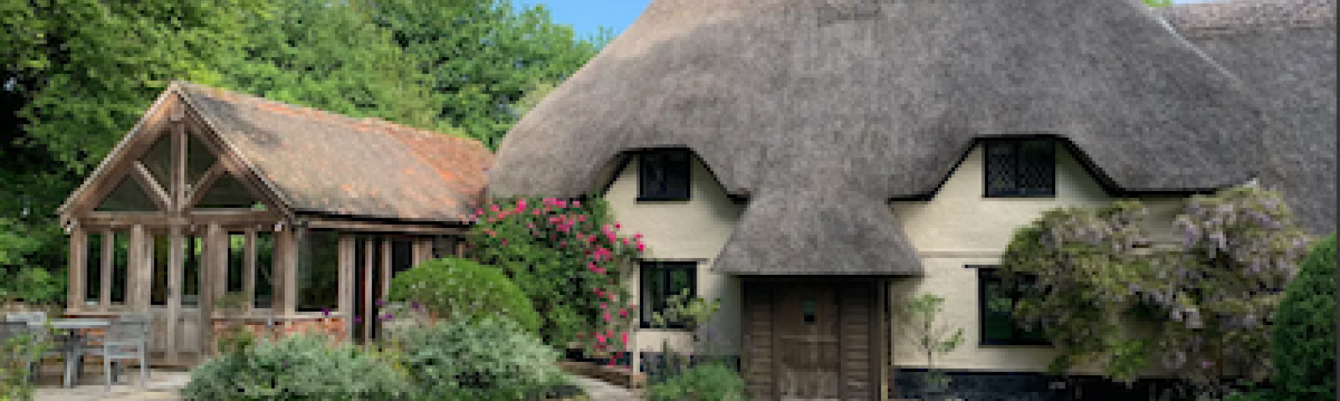 A thatched cottage with thatched porch and large conservatory overlooks a wide lawn.