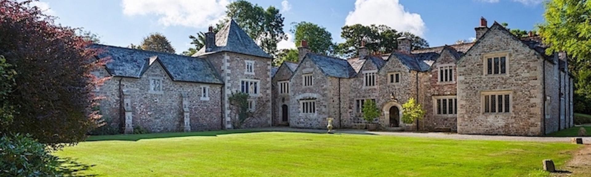 A sprawling Dartmoor Manor house ovrlooks a sweeping, tree-lined lawn.