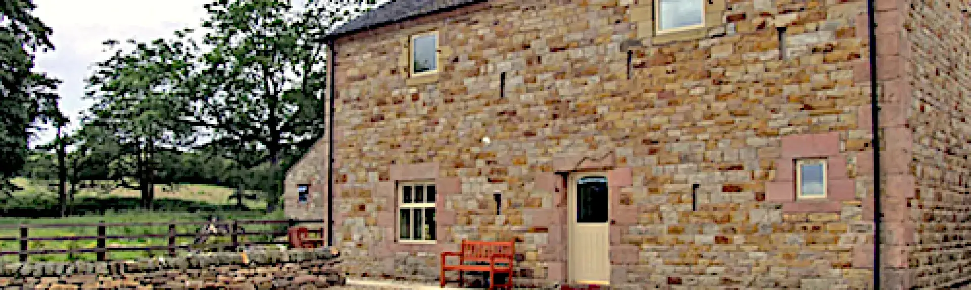 A stone-built, 2-storey Staffordshire barn conversion overlooking a shingled parking area and a fenced-in lawn.