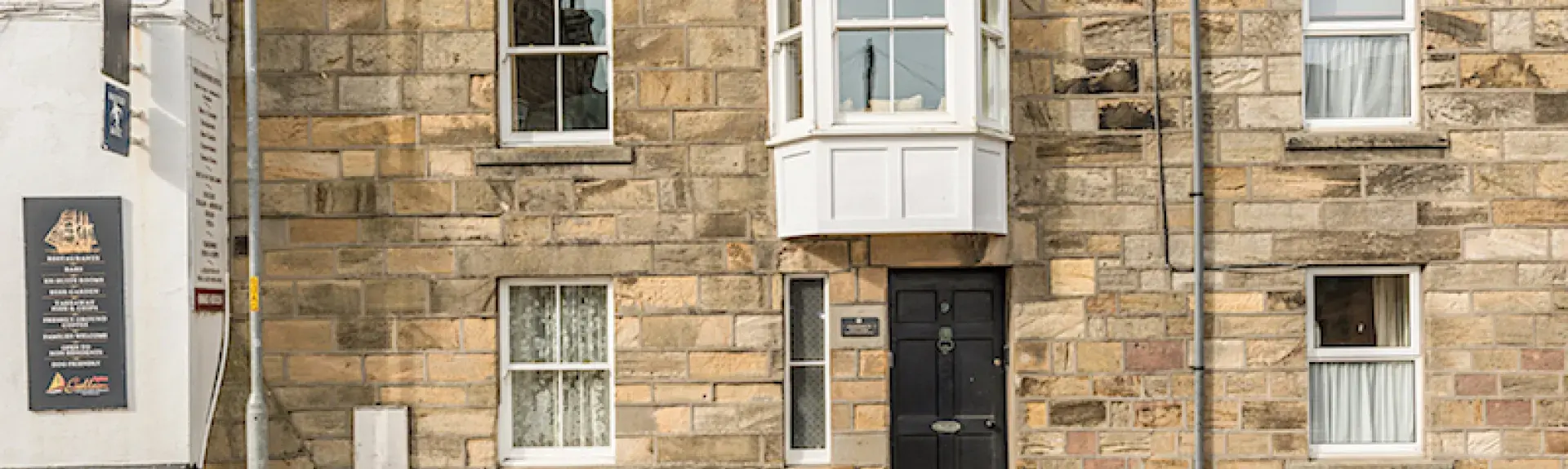 A stone-built terraced cottage with a large, 1st floor bay window overlooks a quiet street.