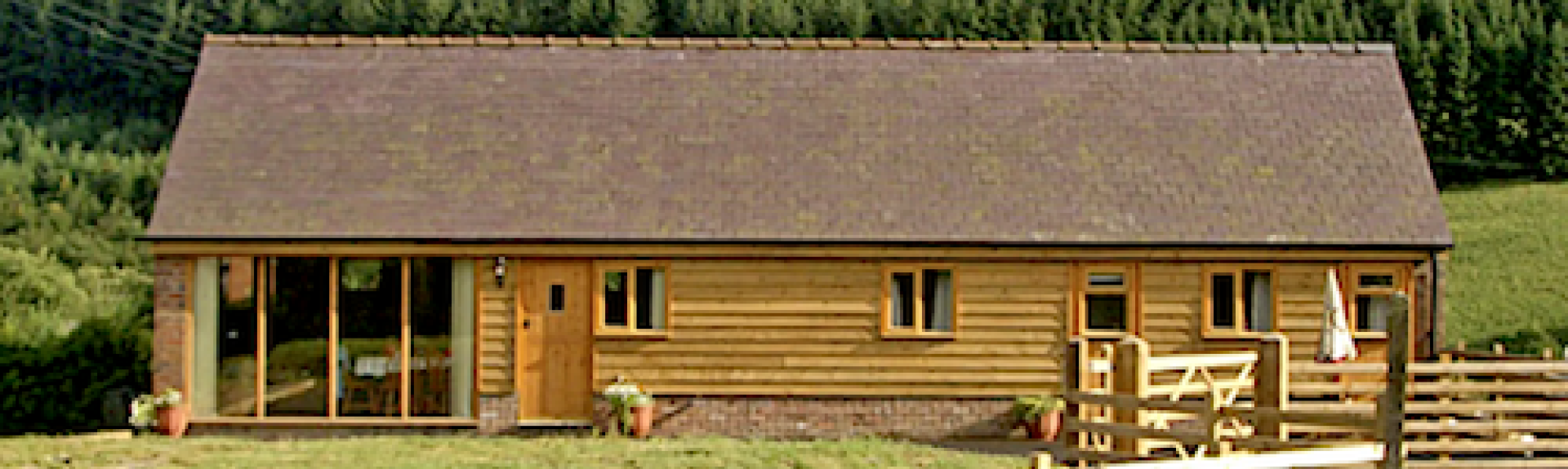 Exterior of a wooden eco-lodge with woods to the rear and open fields in the foreground.