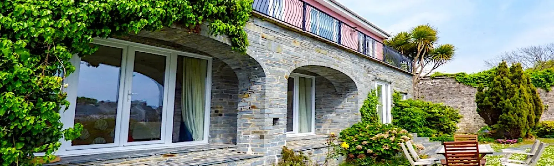 A wisteria-clad Tenby holiday cottage with floor-to-ceiling windows overlooks a daisy-filled lawn.