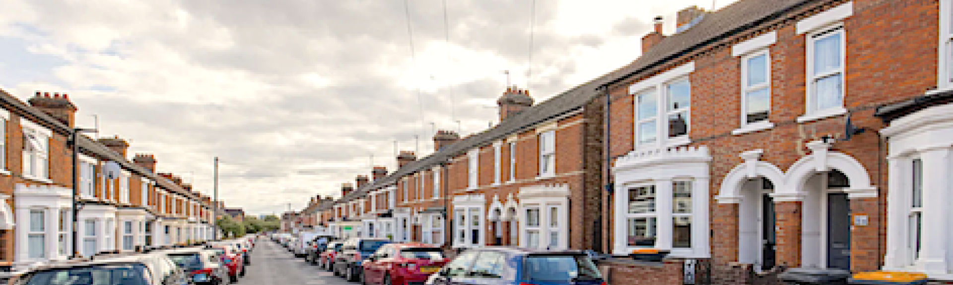 A terrace of brick-built Victorian houses with large bay windows overlook a street.
