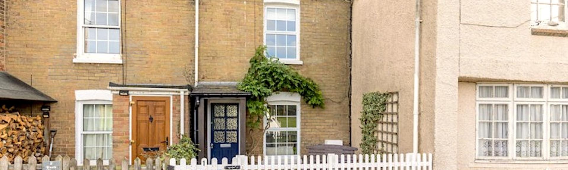 A stone-built terraced cottage with a front garden behind a picket fence.