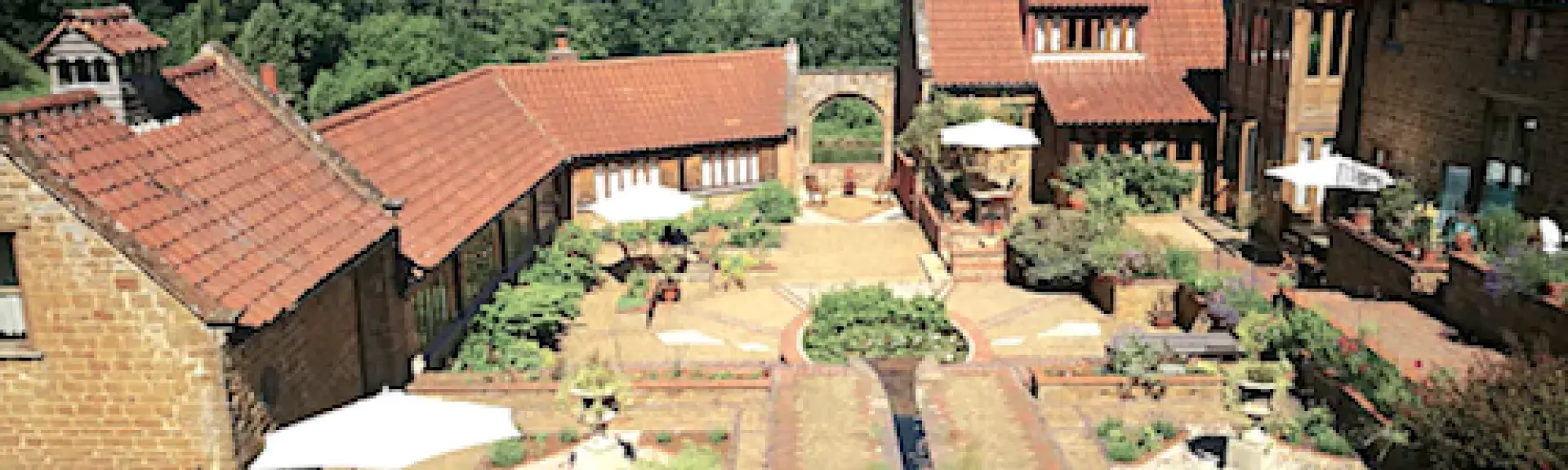A flower-filled, paved formal garden courtyard surrounded by large and small barn conversions