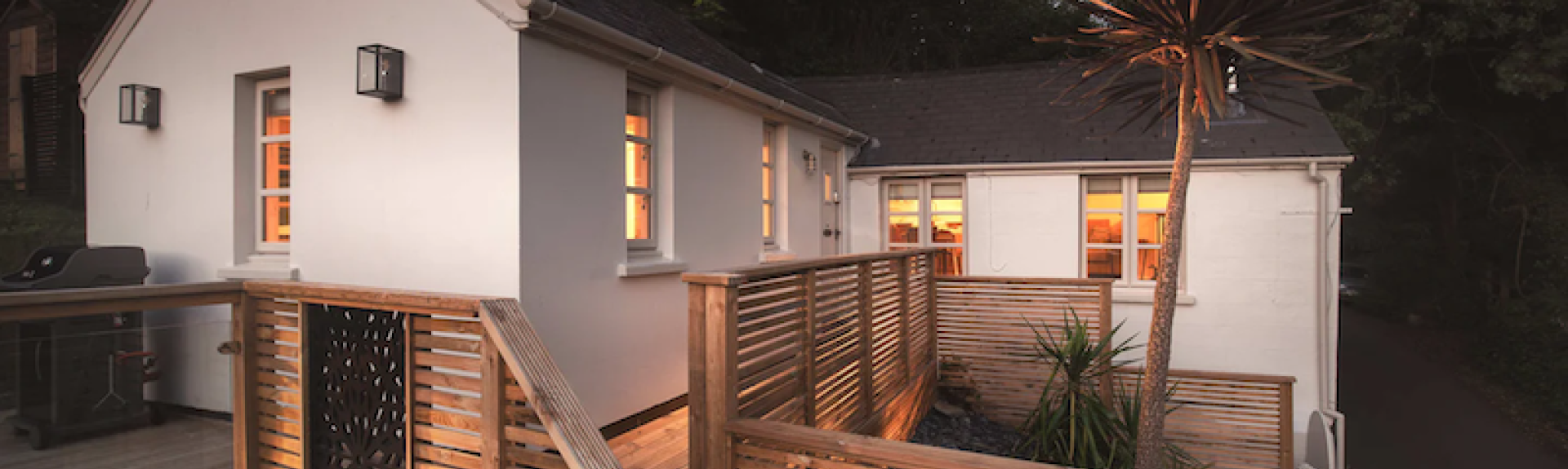A modern Ilfracombe holiday cottage surrounded by a split level wooden deck at dusk.