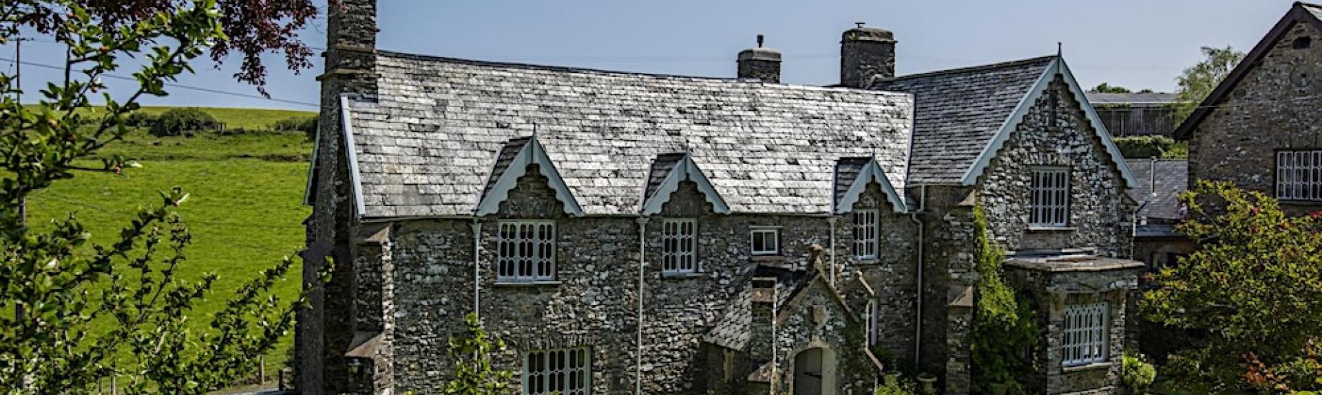 A large stone-built Exmoor cottage surrounded by trees and open fields.