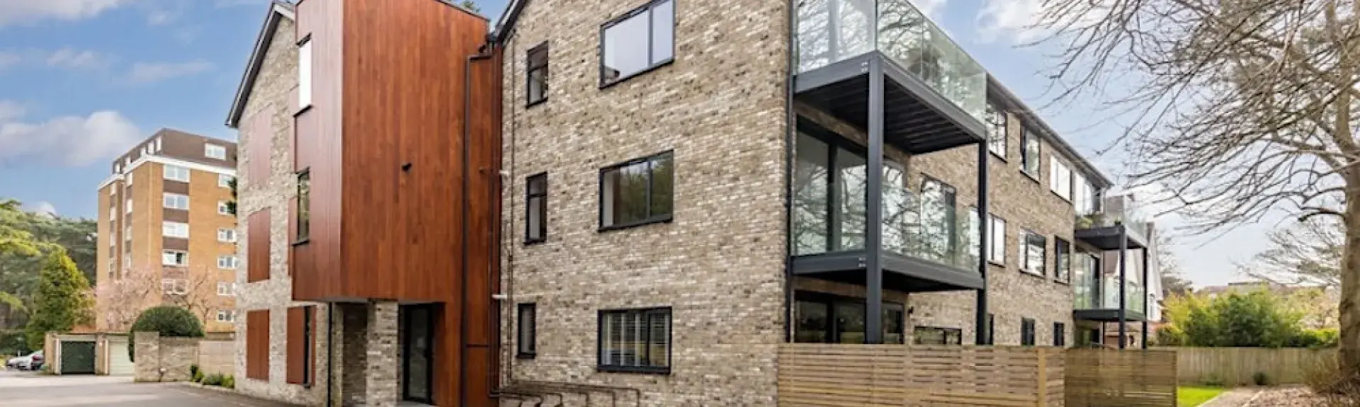A Modern 3-storey apartment block with large glass-fronted balconies with outdoor dining furniture.