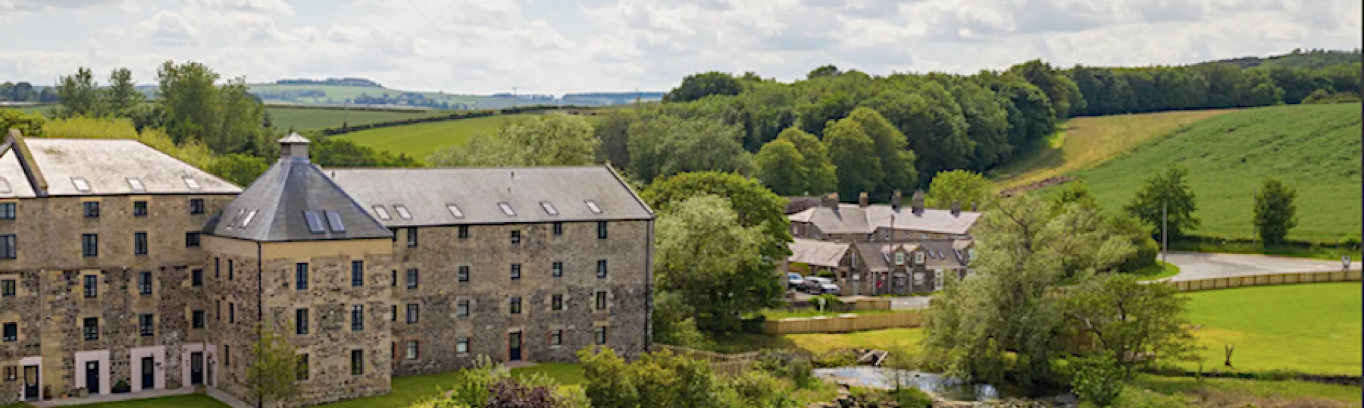 A converted 3-storey mill building overlooking lawns and a lake.